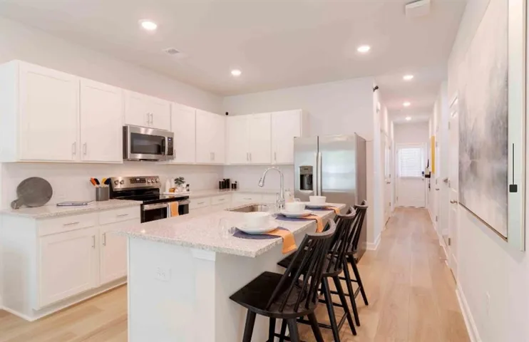 Kitchen with stainless steel appliances, white cabinets, a kitchen breakfast bar, light wood-style floors, and light stone counters