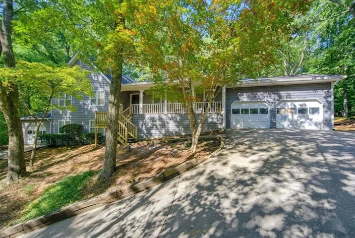Two-car garage with white paneled doors, expansive driveway, and front porch with wood railing