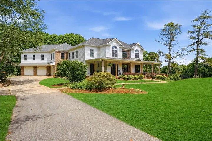 Grand facade featuring white siding,  brick accents, wrap-around covered porch and oversized 3 car garage