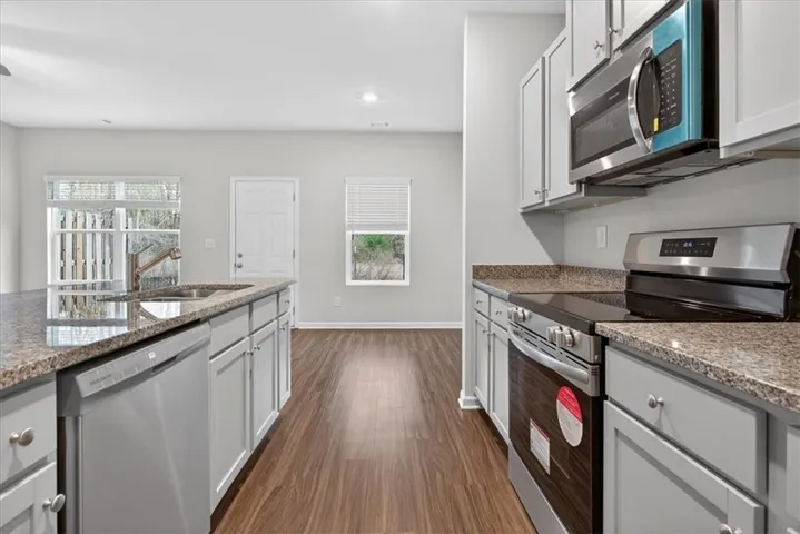 Kitchen featuring light gray cabinetry, stainless steel appliances, speckled stone countertops, and wood-finish flooring