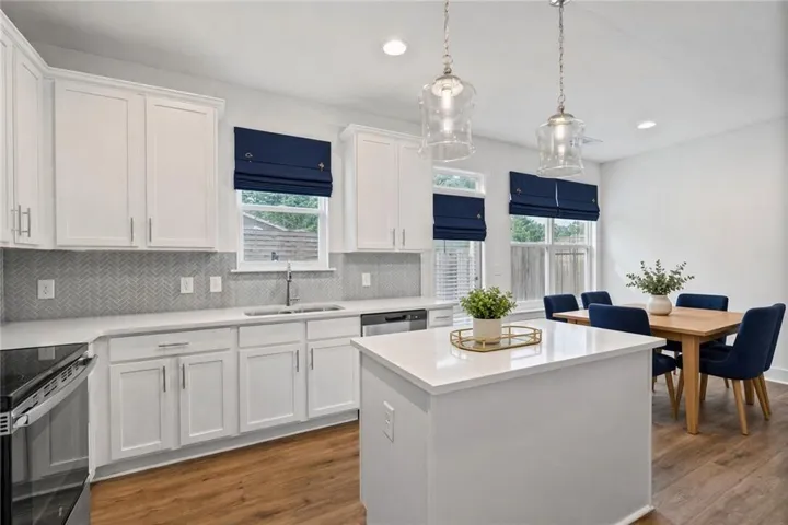 Virtually staged - White shaker-style cabinetry, quartz countertops, a herringbone tile backsplash, and wood-finish flooring