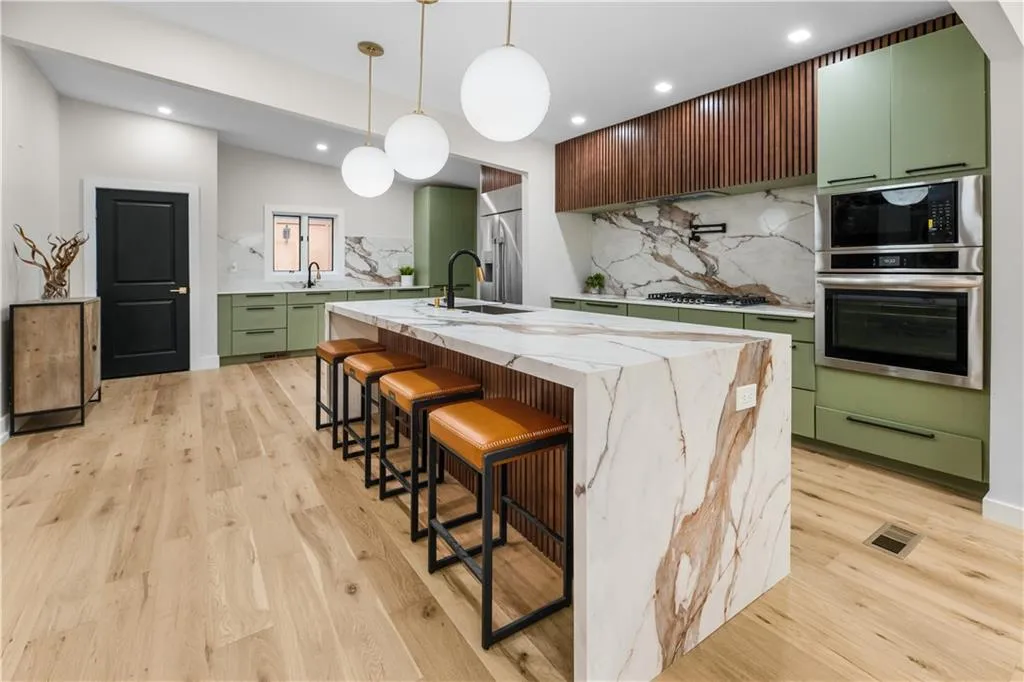 Kitchen featuring green cabinetry, appliances with stainless steel finishes, a kitchen island with sink, light wood-style flooring, and backsplash