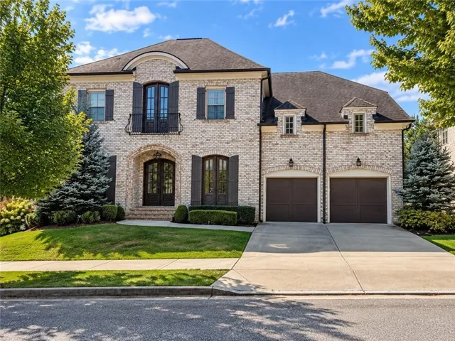 Light brick exterior with dark shutters, arched entryways, a Juliet balcony, and a two-car garage