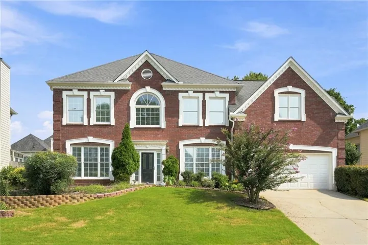 Brick two-story residence featuring a gray shingle roof and a two-car garage
