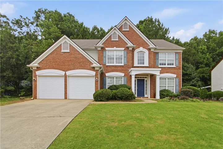 Traditional brick exterior featuring a covered entry, two-car garage, established landscaping, and a manicured lawn