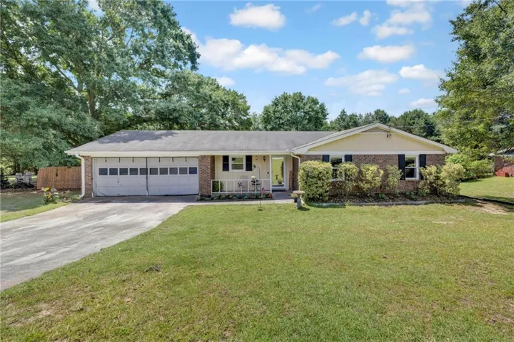 Brick-front ranch style residence with a two-car garage, established landscaping, and a paved driveway