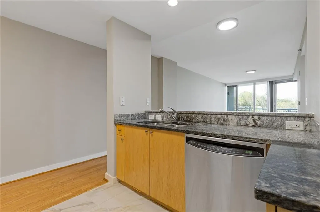 Kitchen with stainless steel dishwasher, light marble finish floors, recessed lighting, and dark stone counters