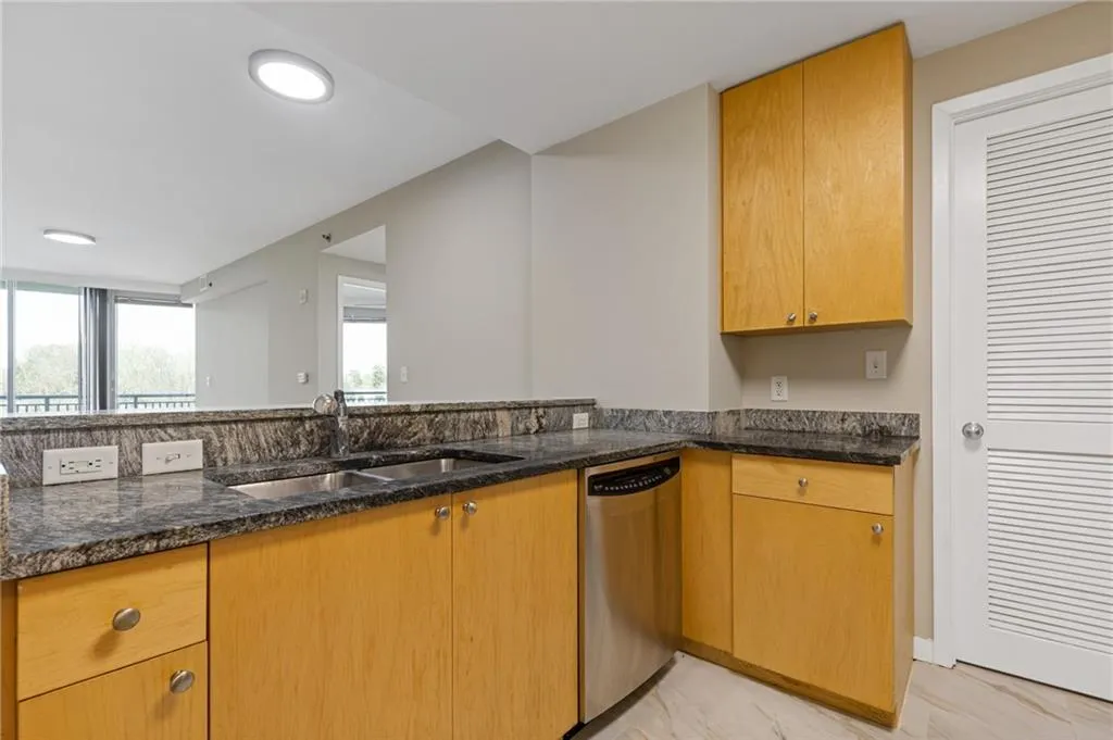 Kitchen with stainless steel dishwasher, dark stone countertops, light marble finish flooring, and recessed lighting