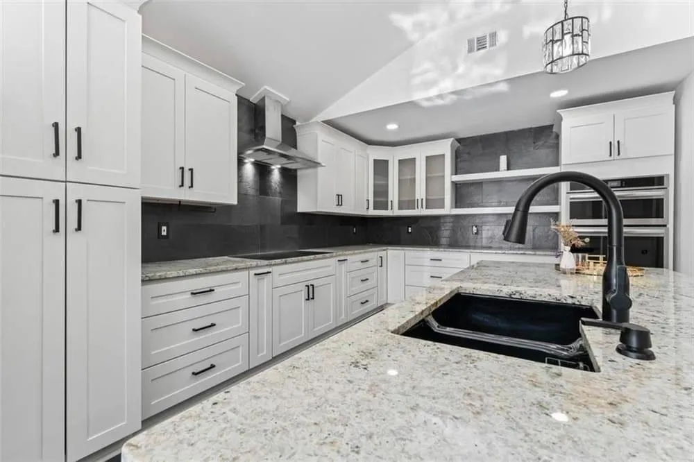 Kitchen with white cabinets, light stone countertops, wall chimney exhaust hood, open shelves, and lofted ceiling