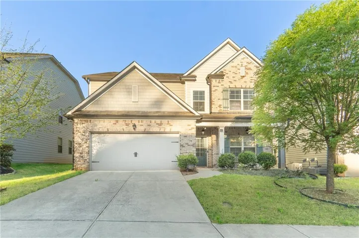 Two-story home featuring a stone and siding exterior with peaked rooflines, two-car garage with white paneled door, and manicured front lawn with mature landscaping
