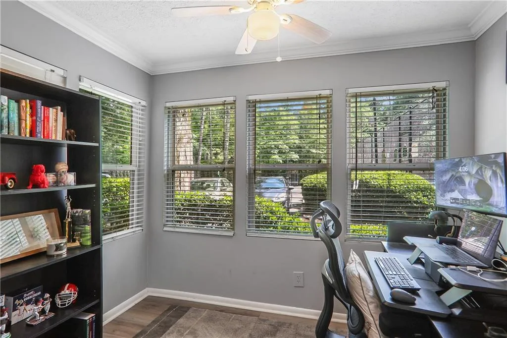 Office area featuring dark wood-type flooring, ornamental molding, ceiling fan, and a textured ceiling
