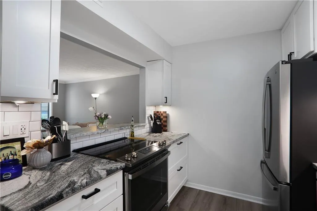 Kitchen featuring dark stone counters, stainless steel fridge, dark wood-type flooring, electric range, and white cabinets