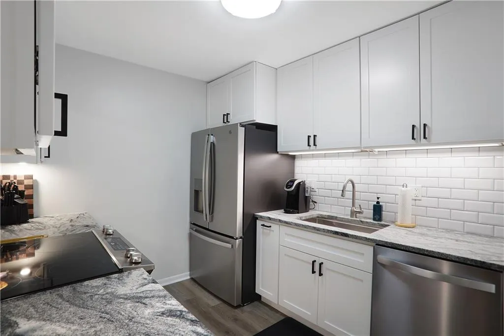 Kitchen featuring stainless steel appliances, white cabinets, hardwood / wood-style flooring, light stone counters, and sink