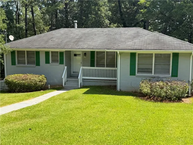 Ranch-style exterior with a light gray facade, green window shutters, and a covered front porch featuring white railings