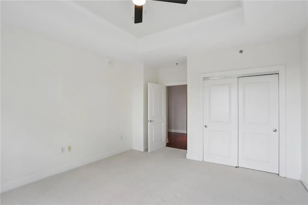 Tray ceiling with crown molding, ceiling fan, white paneled doors, sliding closet doors, and light-toned carpet