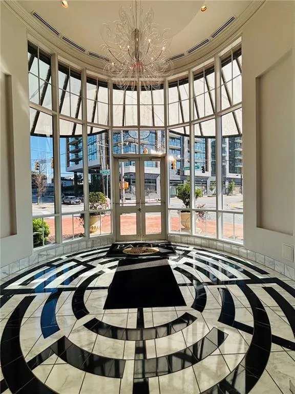 Interior front entryway -Curved window wall with multiple panes, double entry doors, high ceiling, ornate chandelier, and patterned floor tile