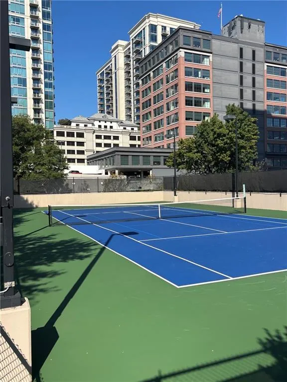 Tennis court with blue playing surface and green surrounds, enclosed by a black chain-link fence