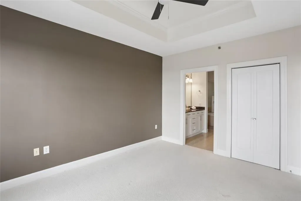 Tray ceiling with a ceiling fan, plush carpeting, and a bi-fold closet door