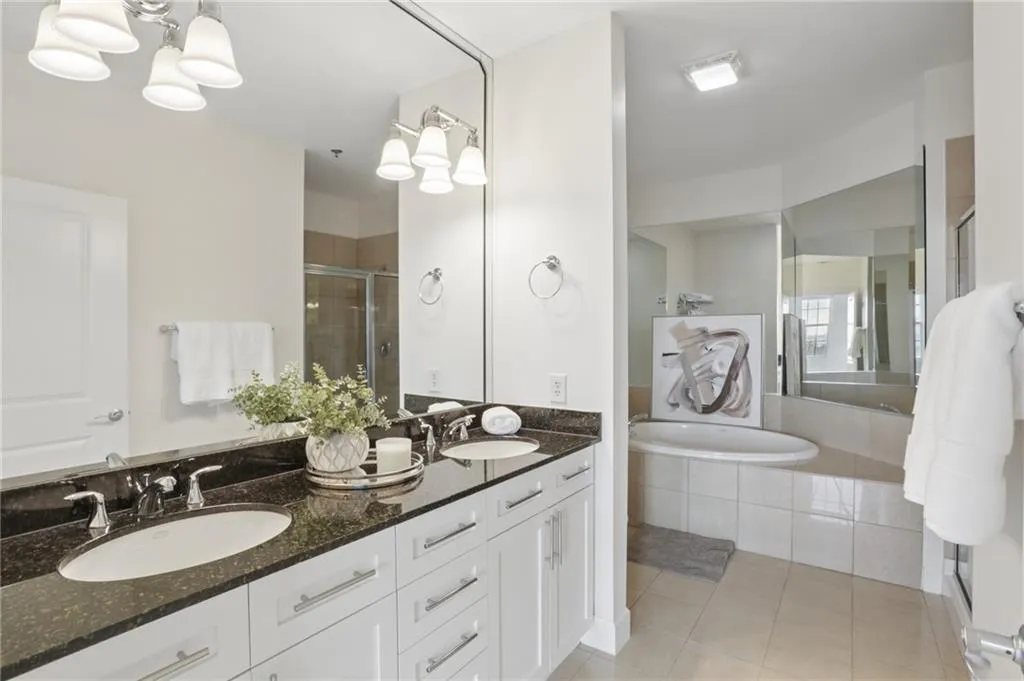 Dual vanity with dark stone countertop, built-in soaking tub, and a glass-enclosed shower