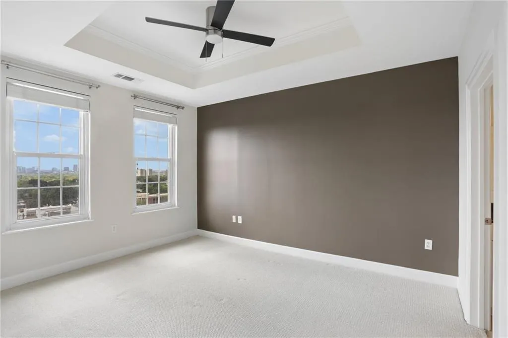 Tray ceiling with a ceiling fan, two windows with blinds, and white carpeting