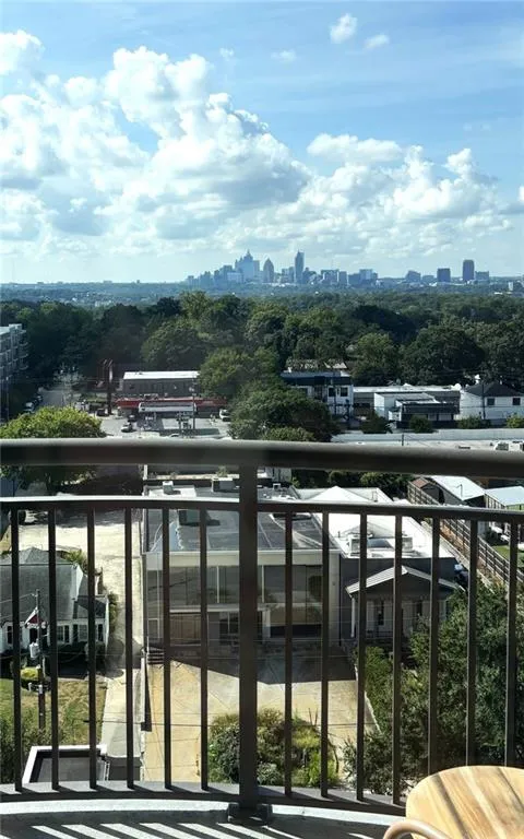 Balcony featuring metal railing, offering a cityscape with distant buildings and expansive green tree canopy