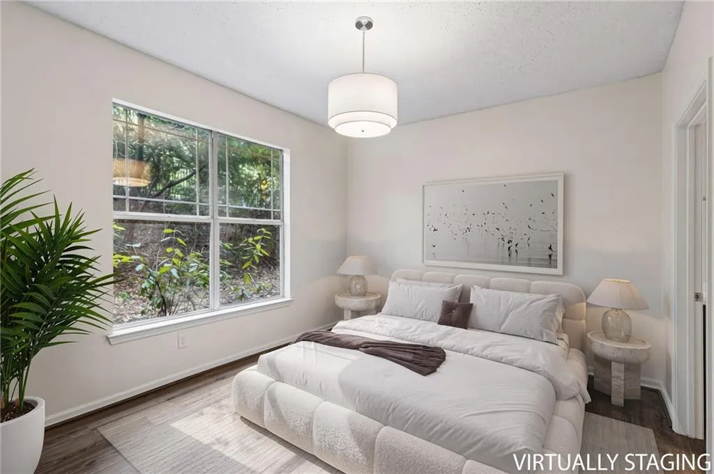 Large window with exterior foliage, wood-finish flooring, and a drum pendant light fixture