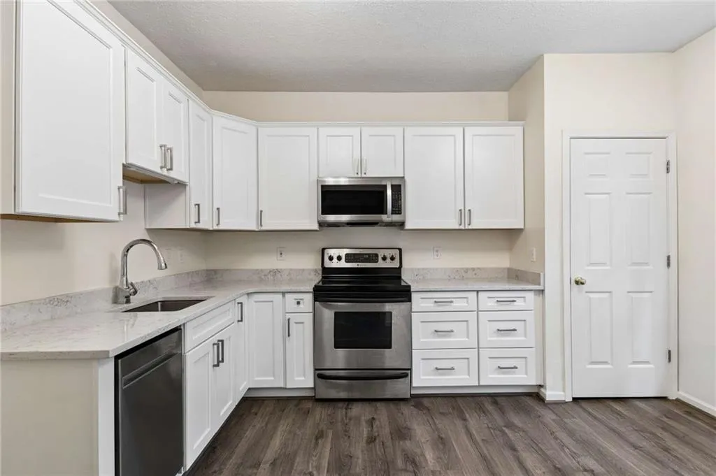 L-shaped kitchen featuring white shaker-style cabinetry, light-toned countertops, stainless steel appliances, and wood-finish flooring