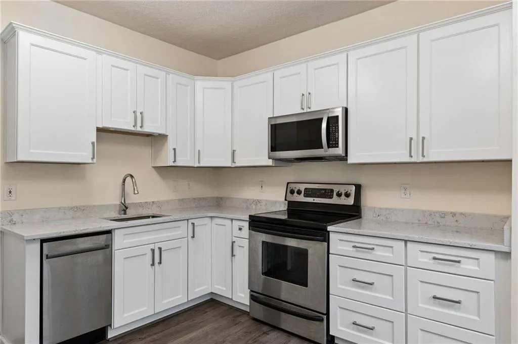 Kitchen featuring white shaker cabinetry, stainless steel appliances, light-toned countertops, and wood-finish flooring