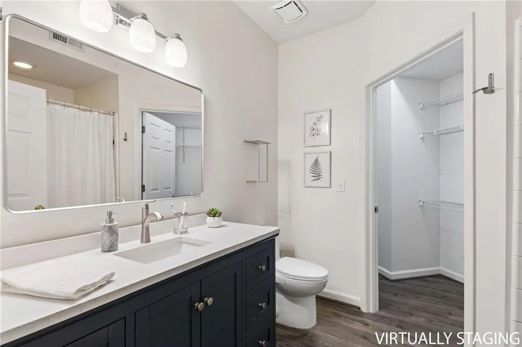 Bathroom featuring a single vanity with a white countertop and dark cabinetry, an undermount sink with a brushed nickel faucet, a rectangular mirror, and wood-finish flooring