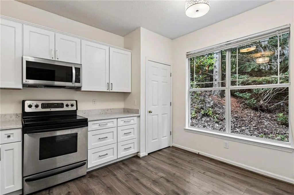 White cabinetry, stainless steel appliances, light-toned countertops, wood-finish flooring, and a large window