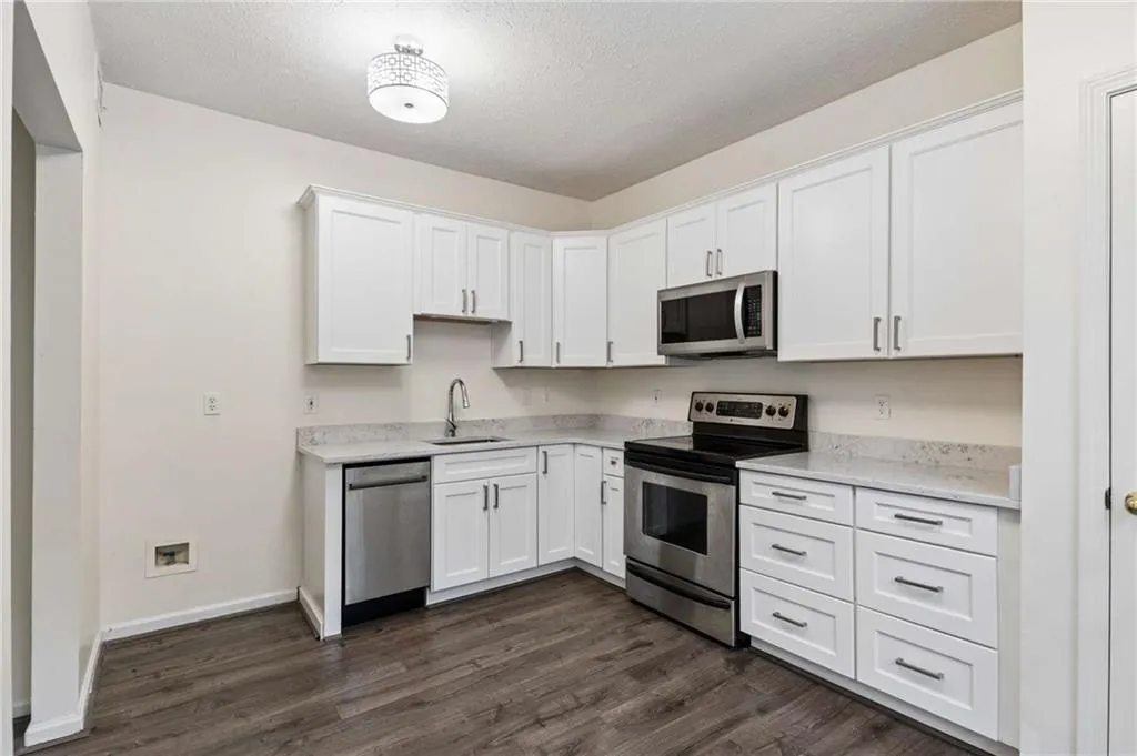 Kitchen featuring white cabinetry, stainless steel appliances, light-toned countertops, a stainless steel sink with a gooseneck faucet, and wood-finish flooring