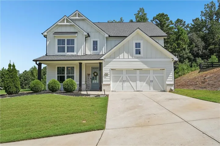 Contemporary farmhouse exterior featuring white siding, a two-car garage with decorative doors, a covered front porch with dark columns, and a concrete driveway