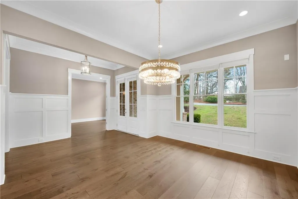 Unfurnished dining area featuring a wainscoted wall, a decorative wall, a chandelier, dark wood-type flooring, and ornamental molding