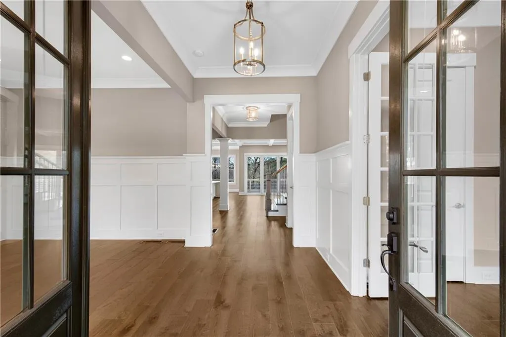 Foyer entrance featuring wainscoting, a decorative wall, ornamental molding, dark wood-style floors, and suspended lighting
