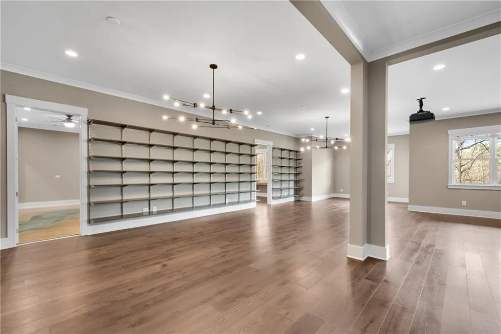 Unfurnished living room with suspended lighting, crown molding, dark wood-type flooring, and ceiling fan