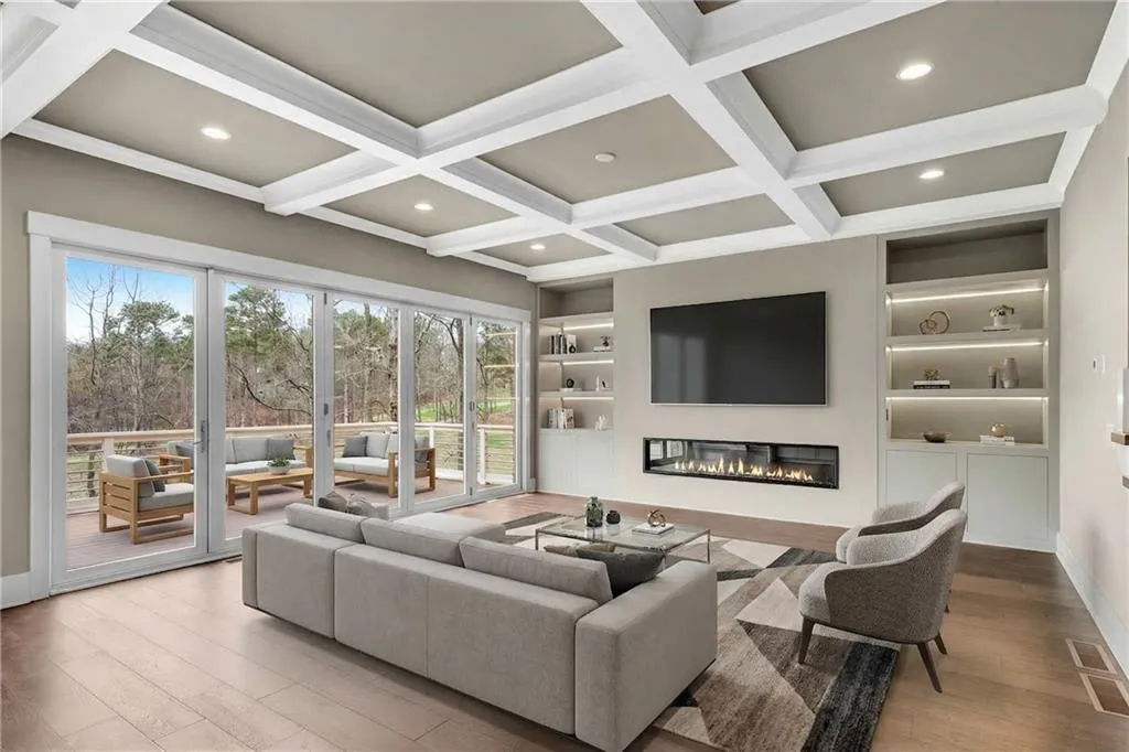 Living area featuring built in shelves, a glass covered fireplace, wood finished floors, recessed lighting, and coffered ceiling