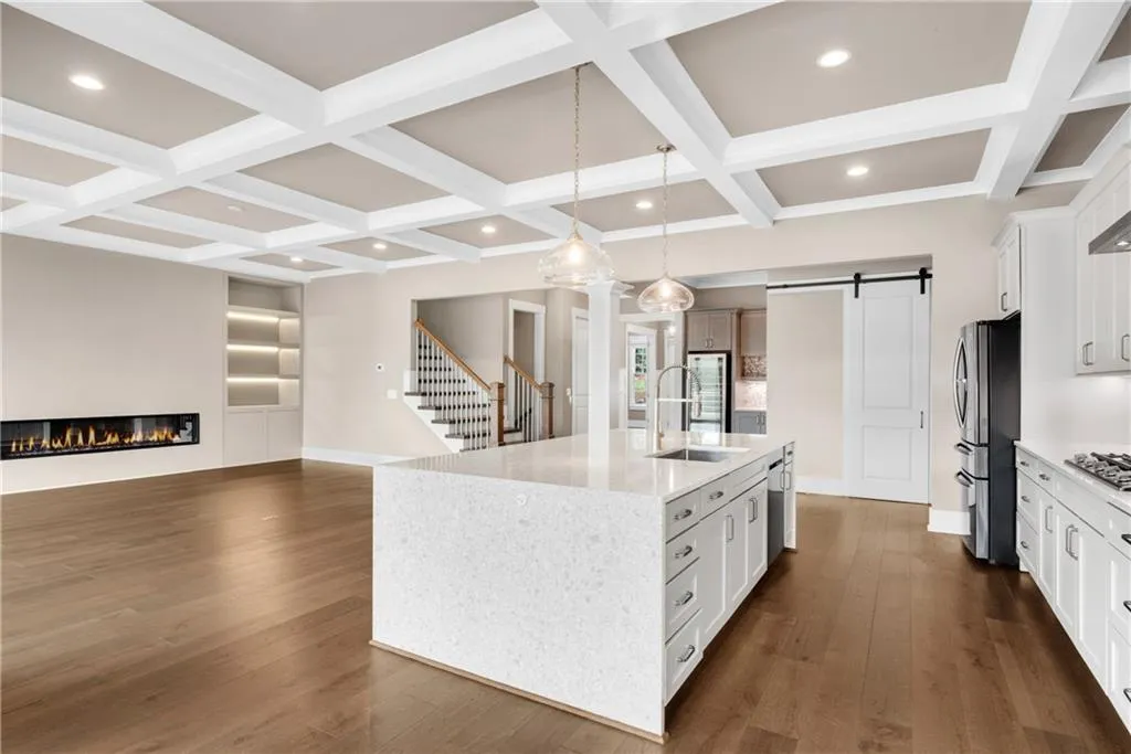 Kitchen featuring a barn door, light stone countertops, a glass covered fireplace, a kitchen island with sink, and pendant lighting