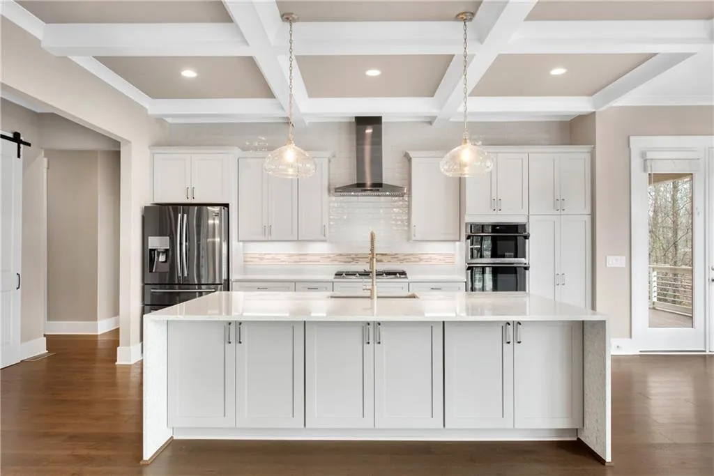 Kitchen featuring a barn door, white cabinetry, light stone countertops, coffered ceiling, and a spacious island