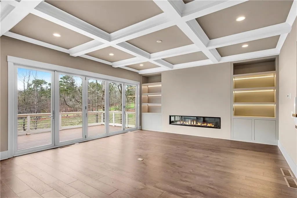 Unfurnished living room featuring built in features, a glass covered fireplace, recessed lighting, wood finished floors, and coffered ceiling
