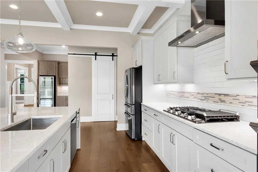 Kitchen with a barn door, light stone countertops, backsplash, beverage cooler, and beamed ceiling