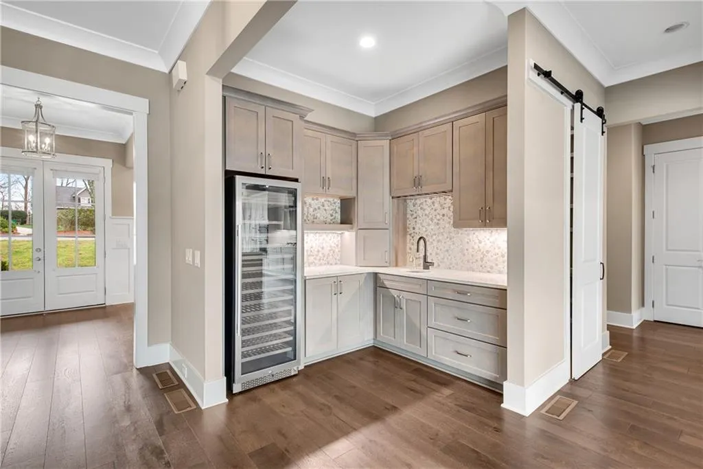 Kitchen with beverage cooler, crown molding, a barn door, dark wood finished floors, and light stone countertops