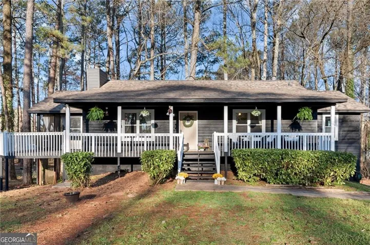 Ranch-style exterior featuring dark siding, a covered front porch with white railings, and mature trees surrounding the property