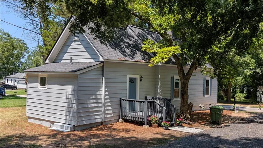 Gable roofline with light gray siding, dark gray front porch, and mature trees