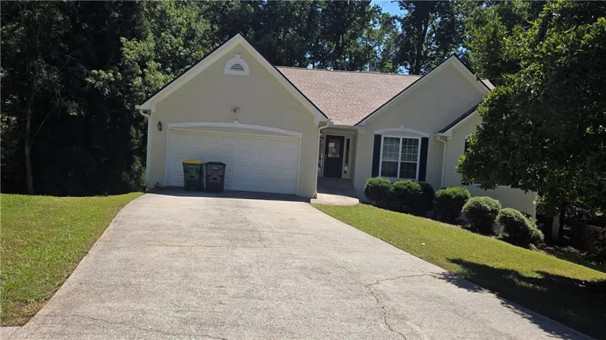 Light stucco exterior with a two-car garage, concrete driveway, and mature landscaping