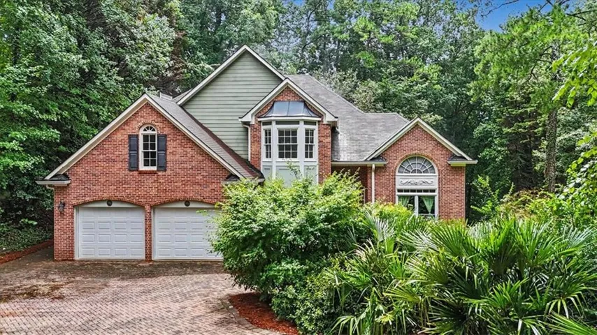 Brick exterior with green siding accents, featuring a two-car garage, bay window, and arched window details