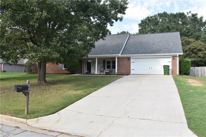 Brick exterior with an attached garage, covered front porch, and mature landscaping