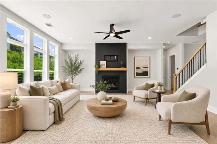 Expansive living area featuring a modern fireplace with a wood mantle, numerous large windows, a ceiling fan, recessed lighting, and wood-finish flooring