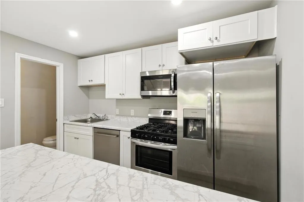 Kitchen featuring stainless steel appliances, white cabinetry, light stone countertops, and recessed lighting