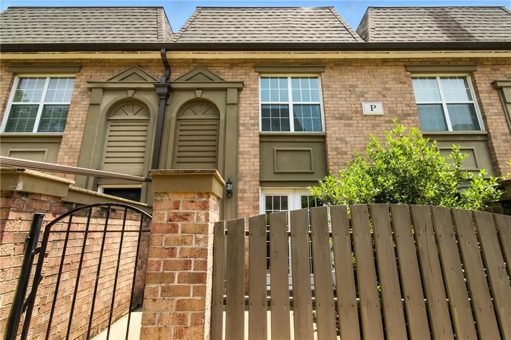 Doorway to property featuring brick siding, a gate, and roof with shingles