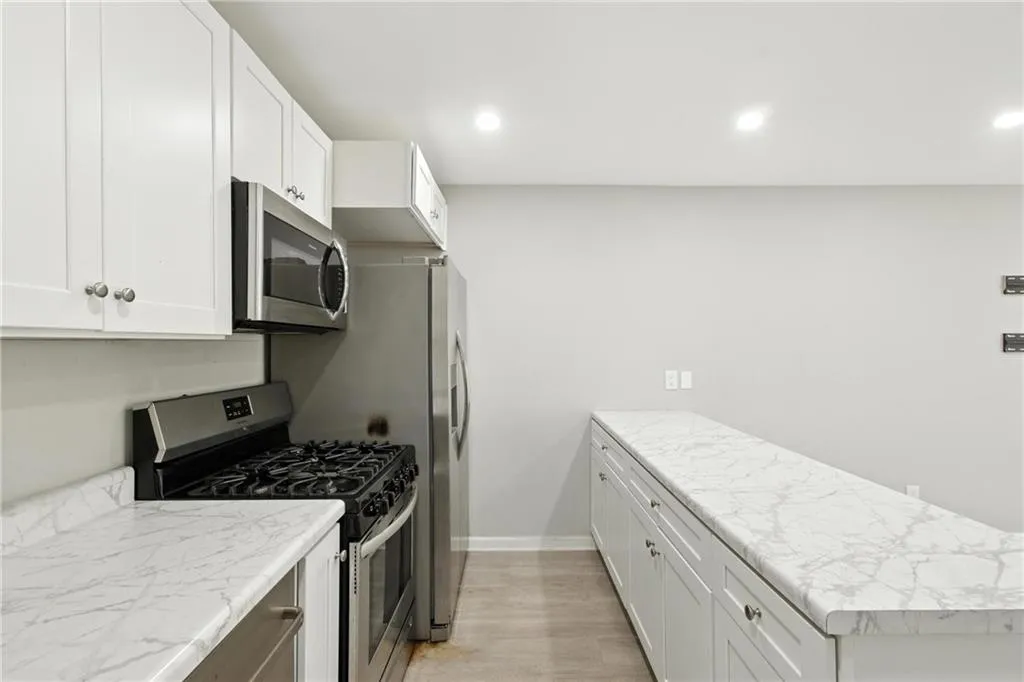 Kitchen with appliances with stainless steel finishes, light wood-style flooring, a peninsula, white cabinets, and recessed lighting
